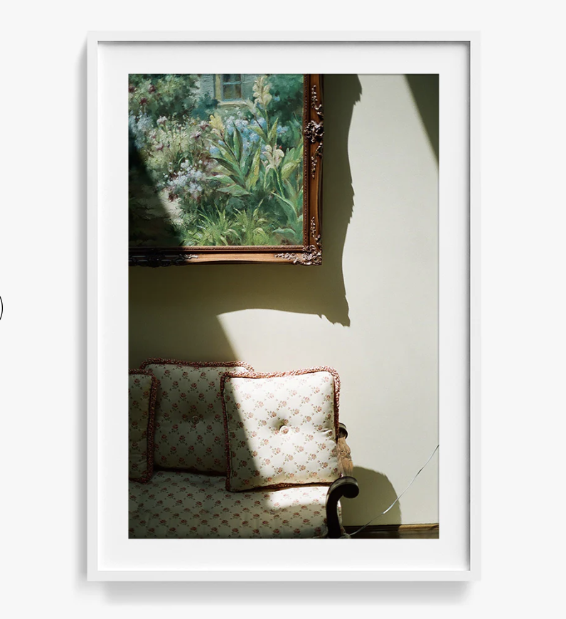 A framed photo of the edge of a couch and corner of a framed painting.