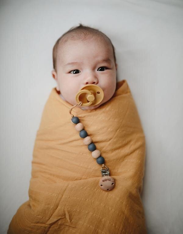 Baby sleeping in a Mushie swaddle blanket.