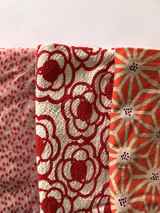 Three fabric swatches in a variety of red patterns. 