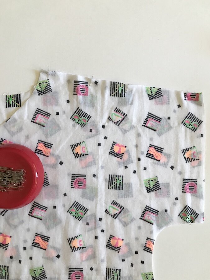 A piece of white patterned fabric with pins in it.