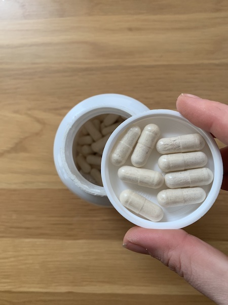 A hand holding a cap full of FullWell prenatal vitamins. 