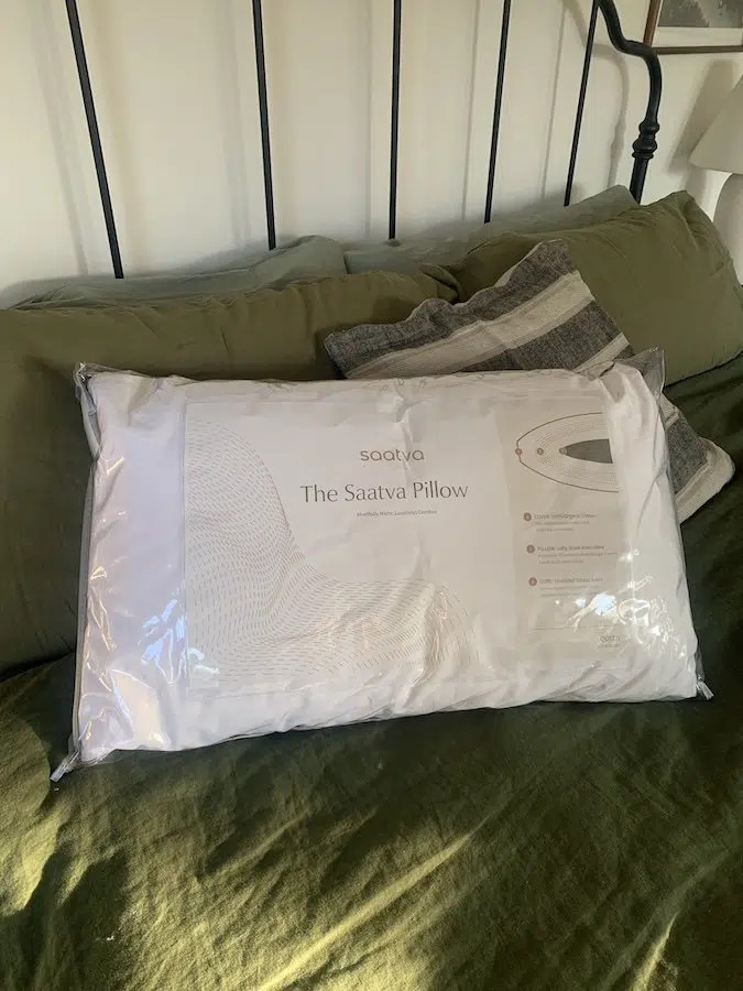 A Saatva pillow in its packaging on a neatly made bed.