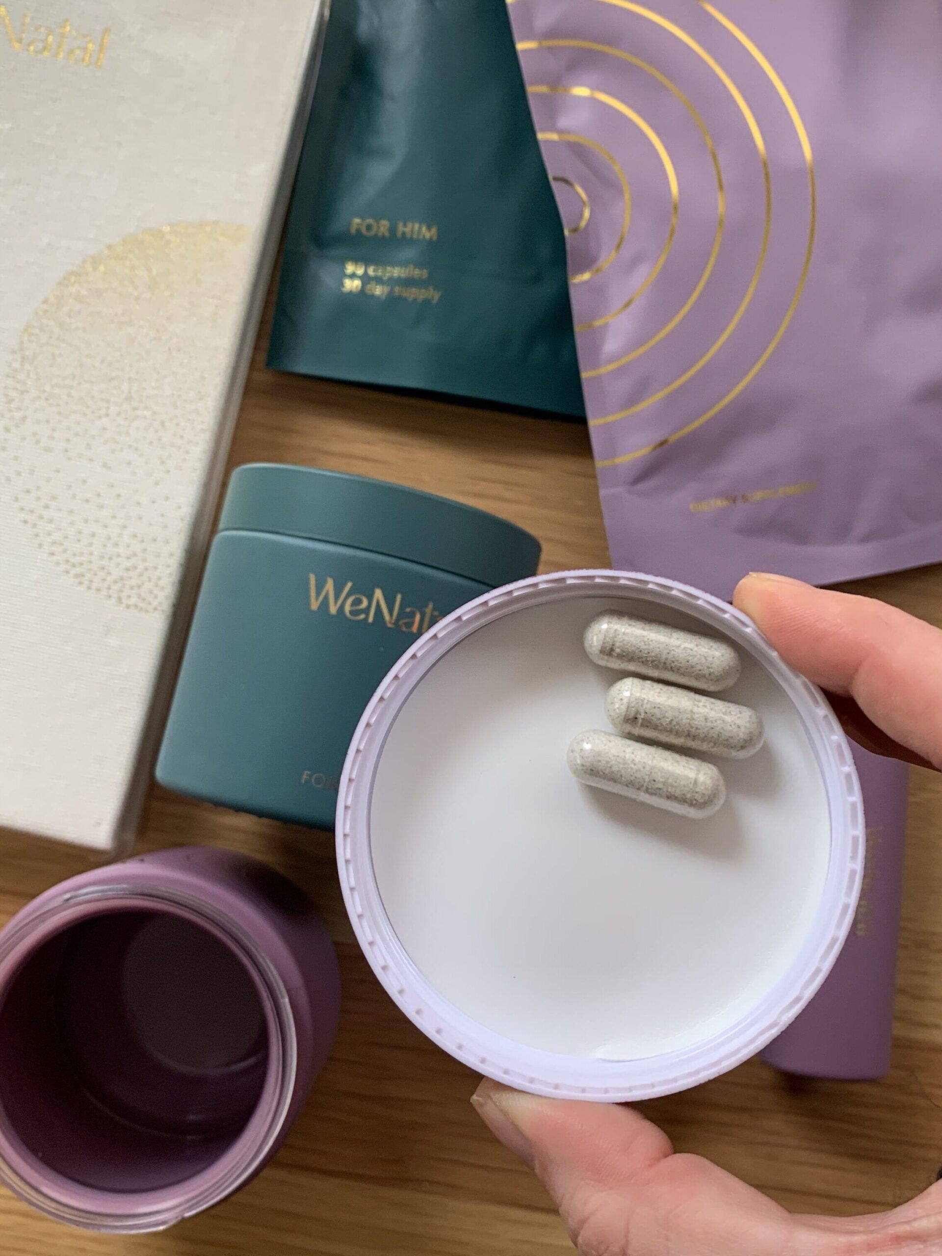 A variety of WeNatal organic prenatal vitamins, with a hand holding a capful of vitamins. 