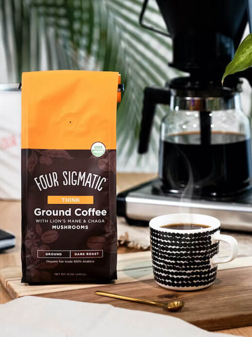 A pack of Four Sigmatic coffee alternative. To the right is a white mug with black spots, filled with a steaming cup of the brewed blend.
