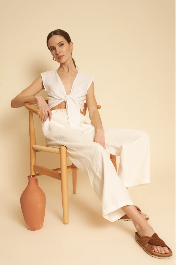 A model lounges in a chair, wearing a white linen set.