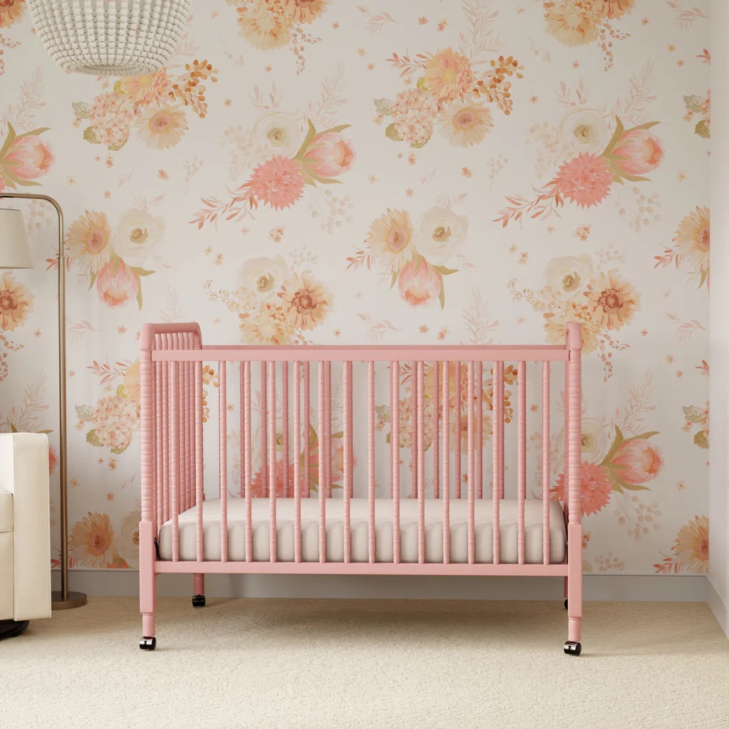 A pink wooden crib in a nursery with floral wallpaper.