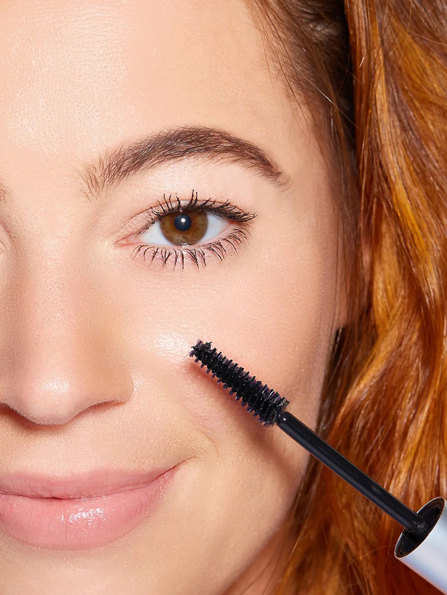 A model holding a mascara wand by their face. 