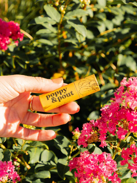 A hand holding a Poppy & Pout Lip Balm. 