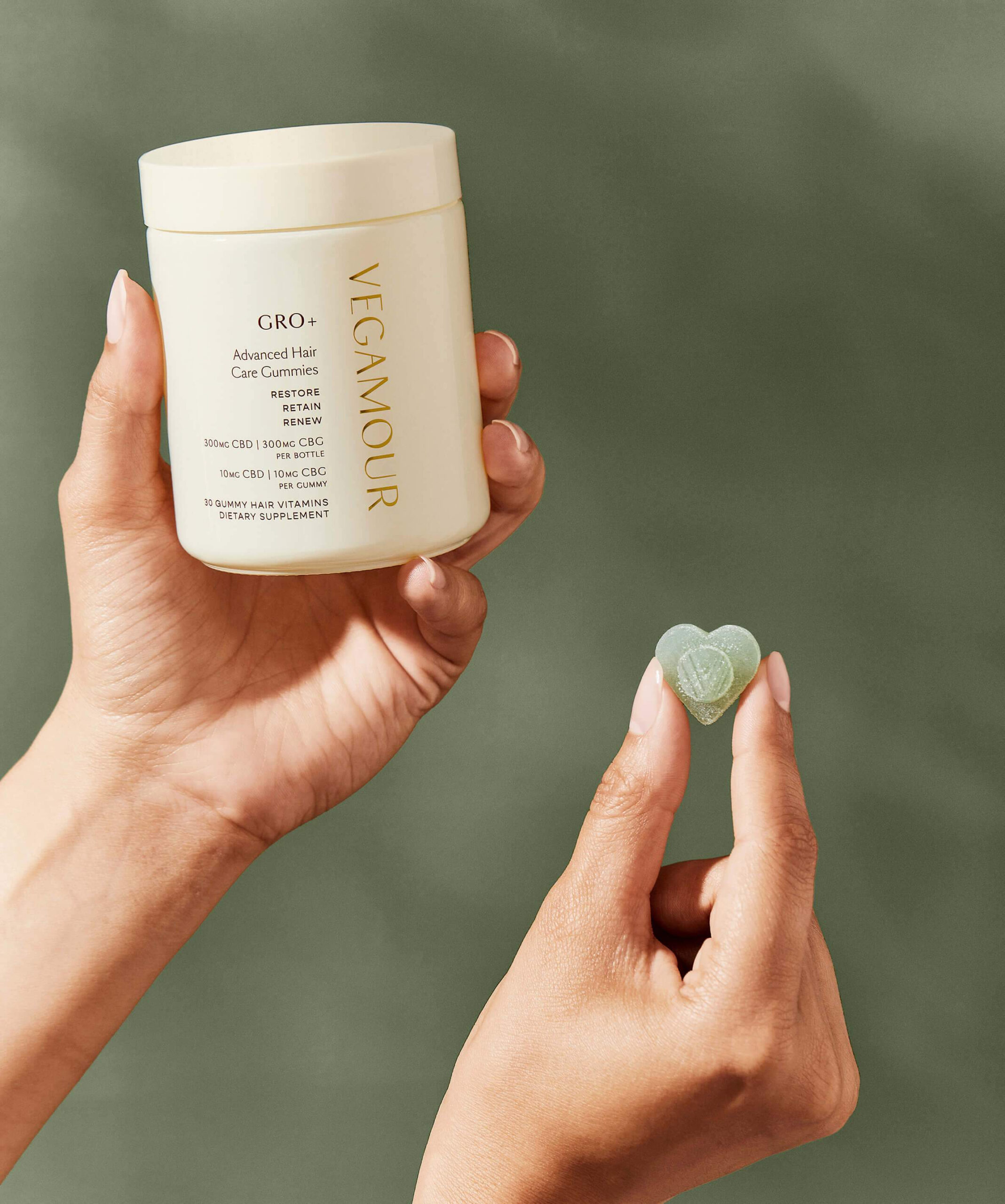 A hand holds a gummie and a package of Vegamour gummies. 