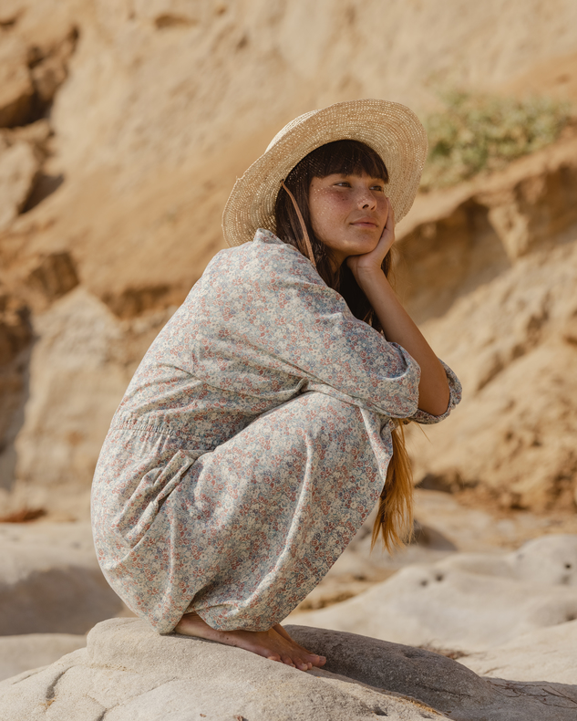 woman in dress and sunhat kneeling sitting down on rocky coastline