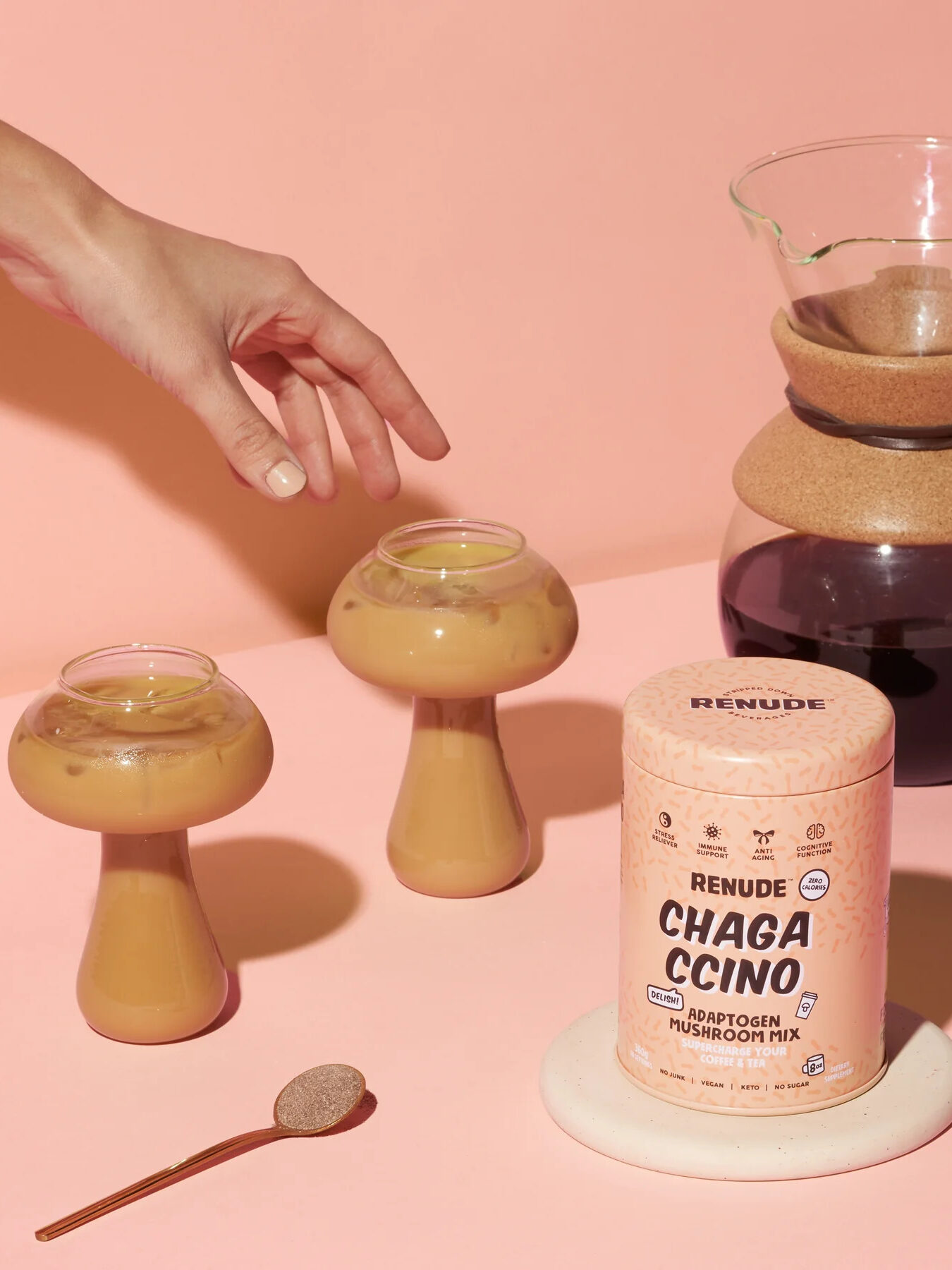 A container of Renude Chagacinno Coffee Alternative. To the left are two glasses shaped like mushrooms filled with the iced brewed blend.