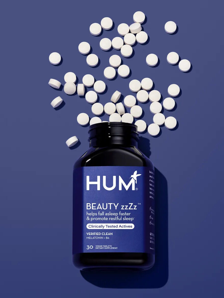 A open bottle of HUM Beauty zzZz melatonin supplements with the tablets scattered .