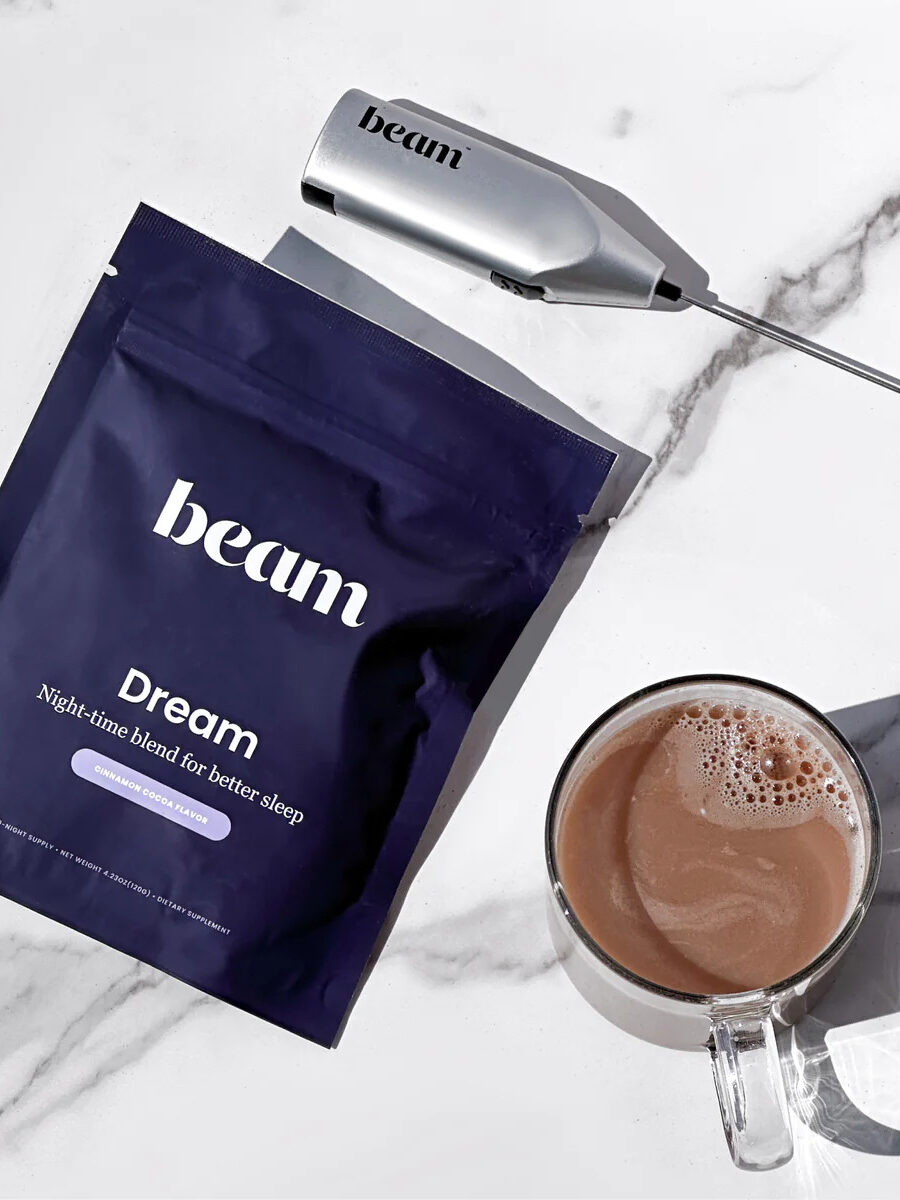 A packet of beam Dream sleep blend powder with a frother and a ready made cup of the mix next to the packet.