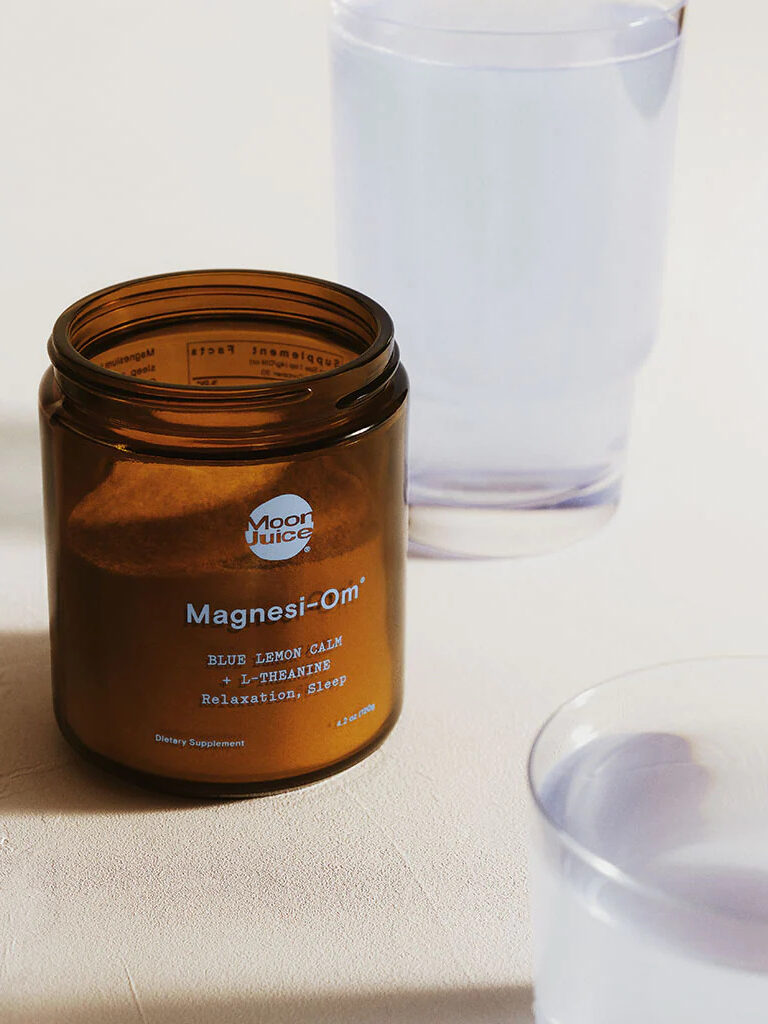 An open jar of Moon Juice Magnesi-om with a glass behind it.