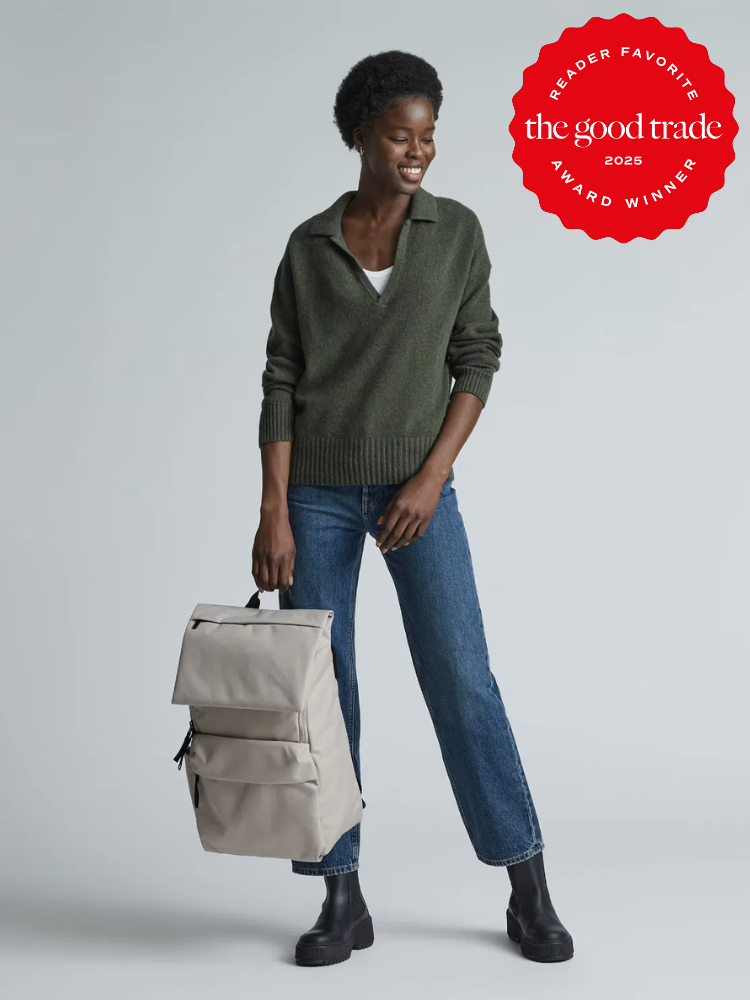 Person in a green sweater and jeans holds a gray backpack, smiling. Red badge on image says "Reader Favorite: The Good Trade Award Winner 2025.