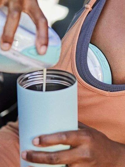 A hand pouring milk from a Willow Breast Pump into a cup.