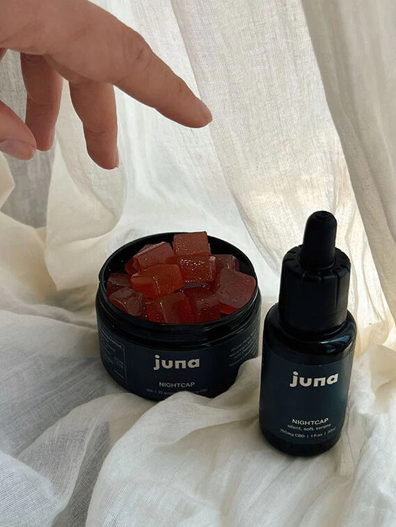 A hand reading for an open jar of Juna Nightcap, with Juna's Nightcap CBD oil next to it.
