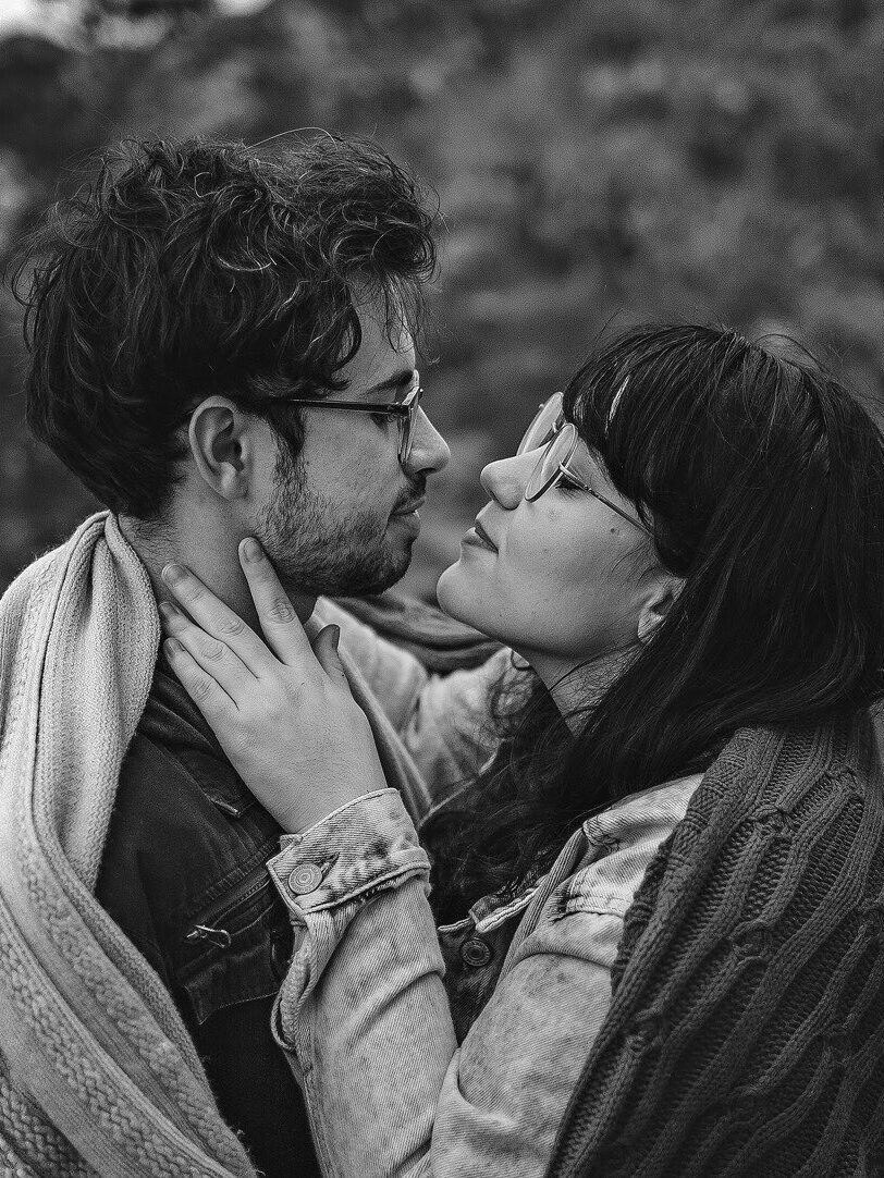 A black and white photo of a couple hugging in the woods.