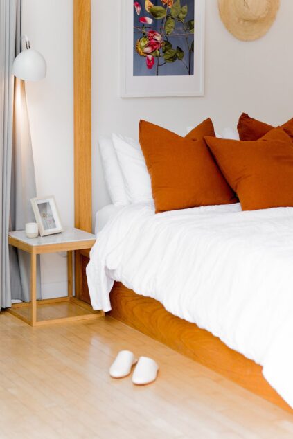 A bed with a natural latex mattress, and a pair of slippers on the floor beneath.