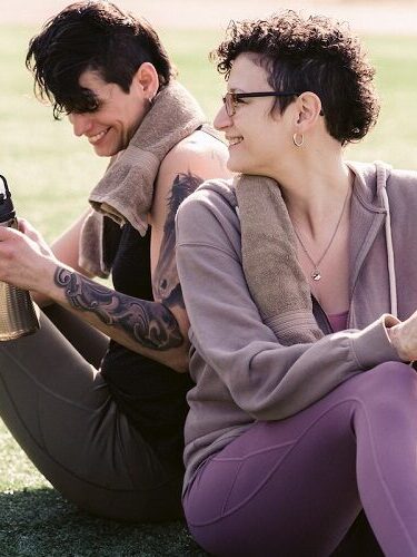 Two women sitting on the grass with water bottles.