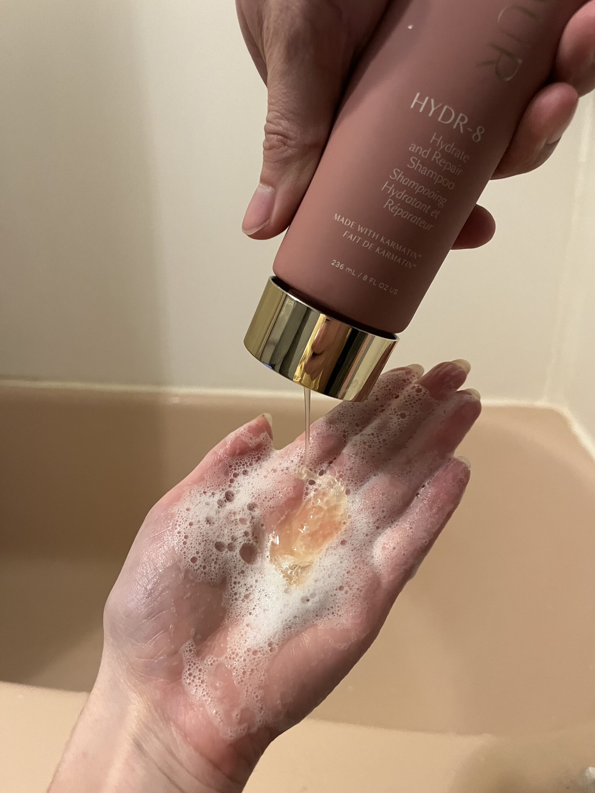 Dispensing shampoo into a hand above a bathtub.