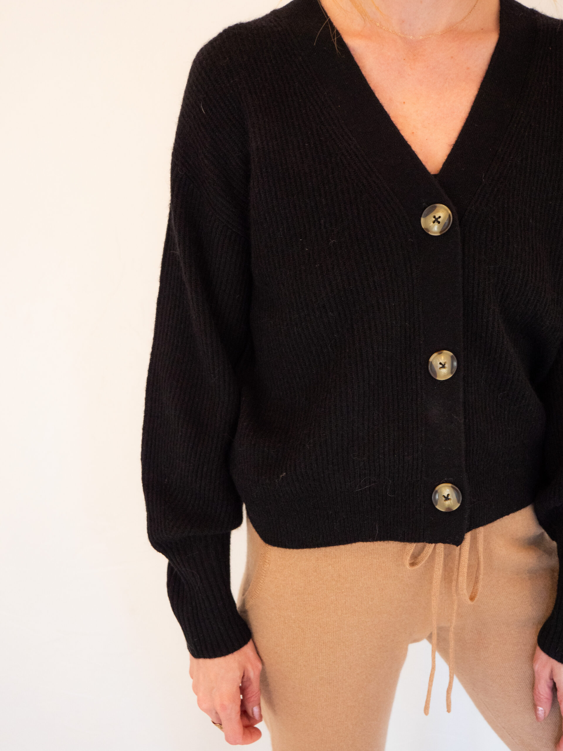 A woman wearing a black cardigan and tan pants.