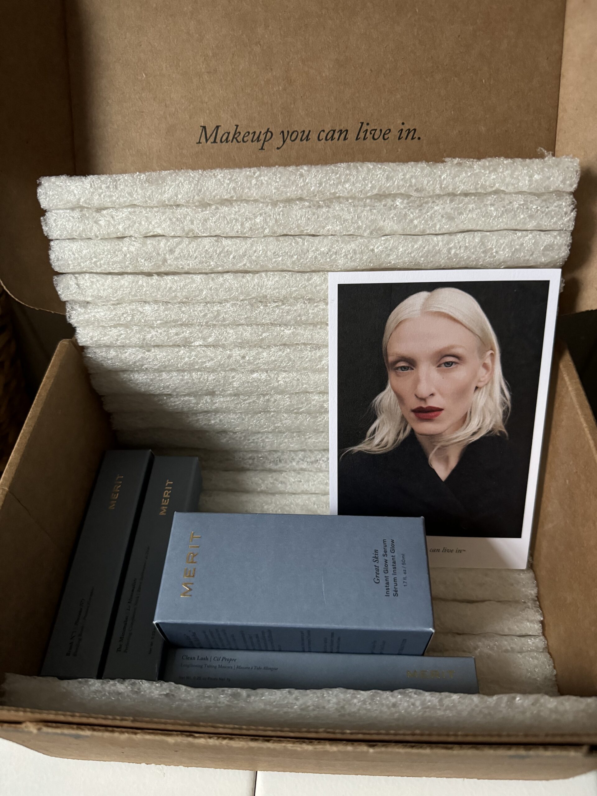 A makeup product package with a promotional image of a model and several boxed items inside a cardboard box.