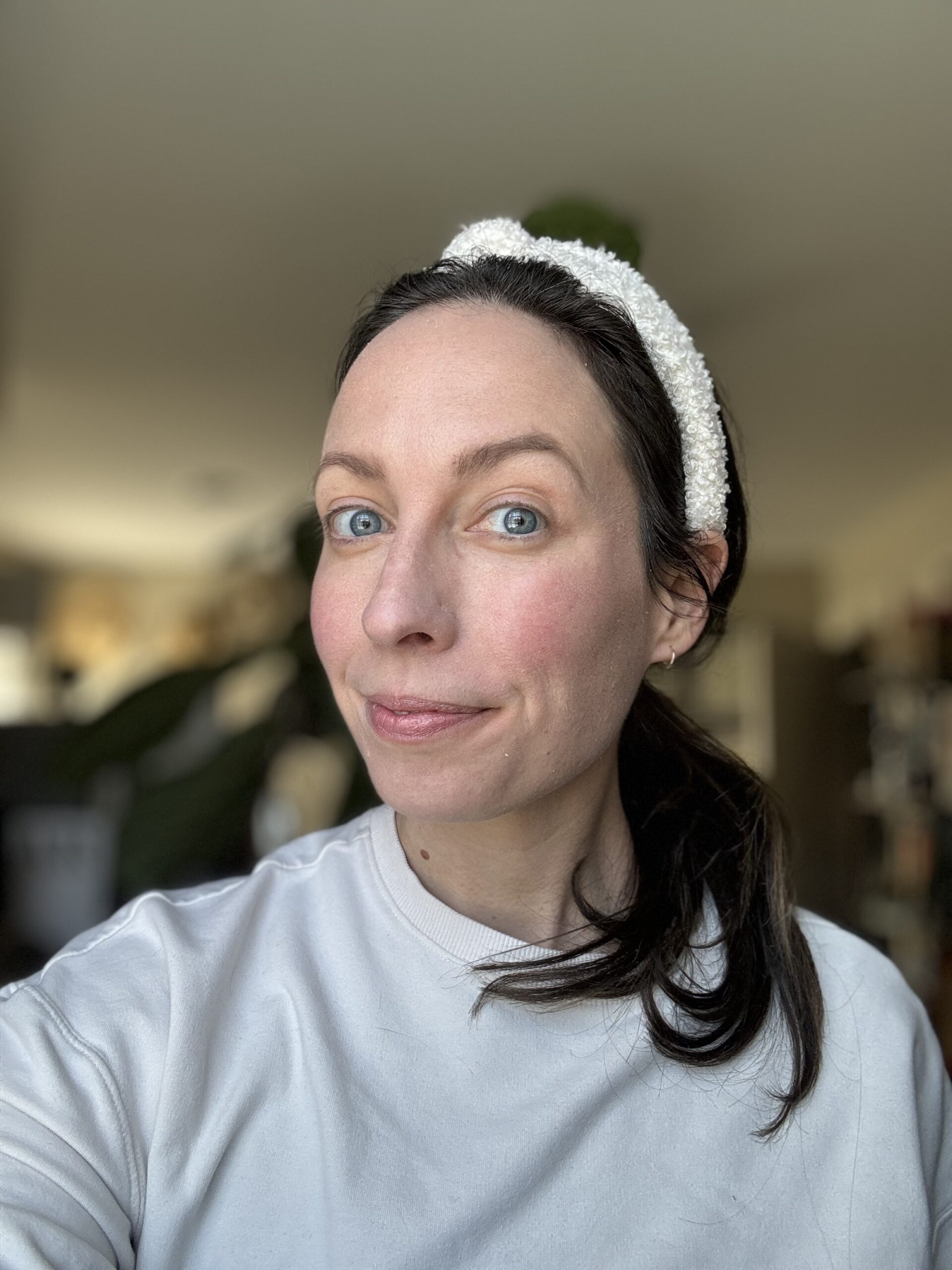 Woman with blue eyes wearing a white headband and a white top, slightly smiling at the camera.