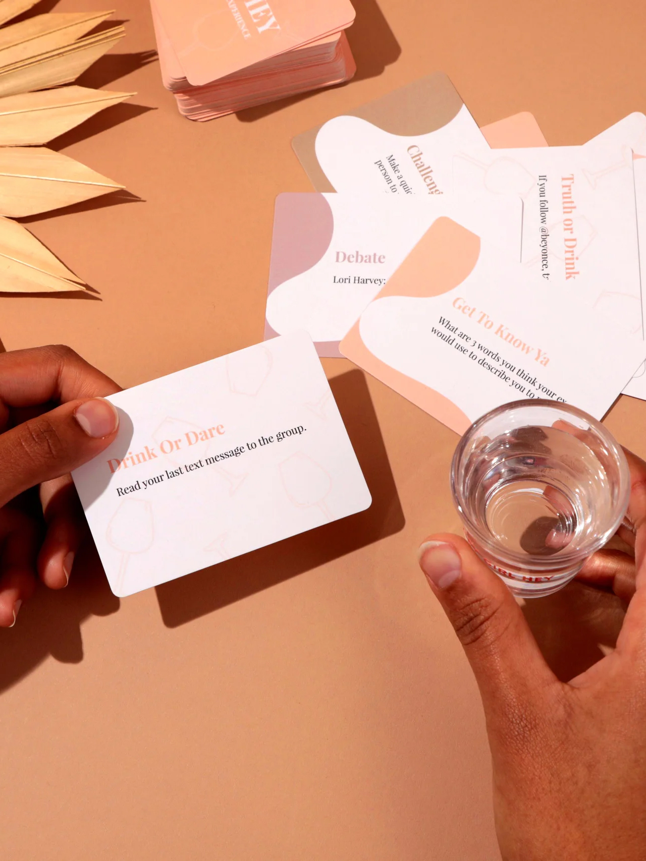A hand holding a 'drink or dare' card above a table with various game cards spread out and an empty glass.