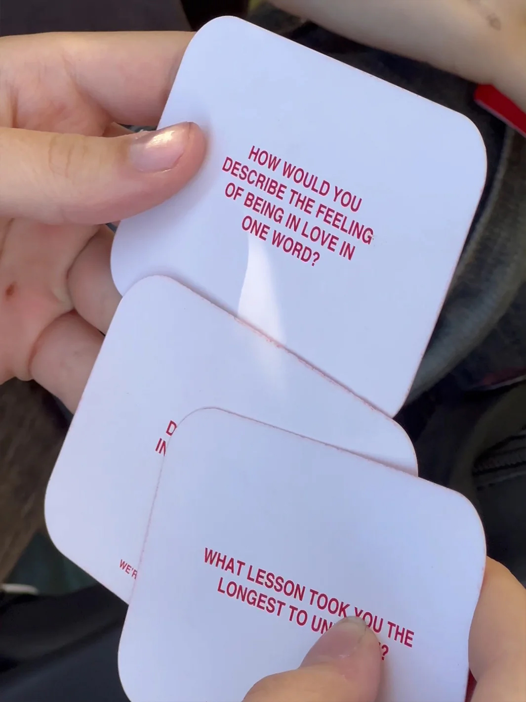 Hands holding conversation starter cards with reflective questions on love and life lessons.