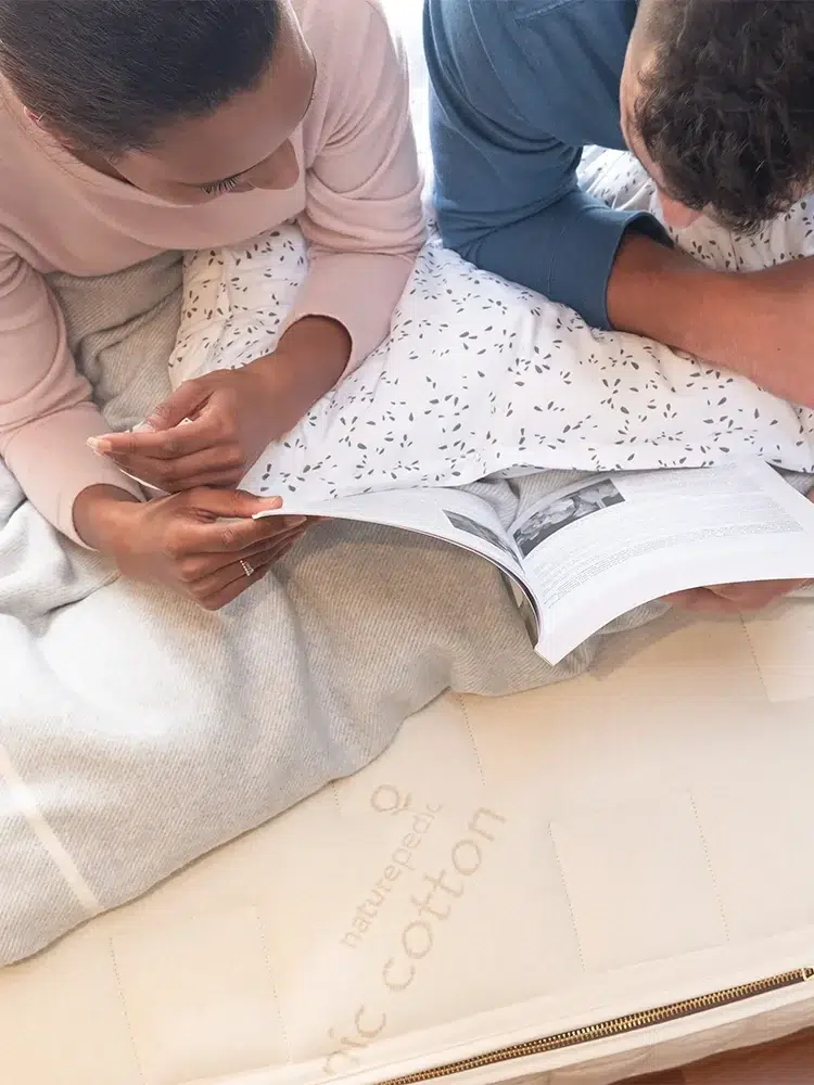 Two people lay on a Naturepedic mattress, reading a book.