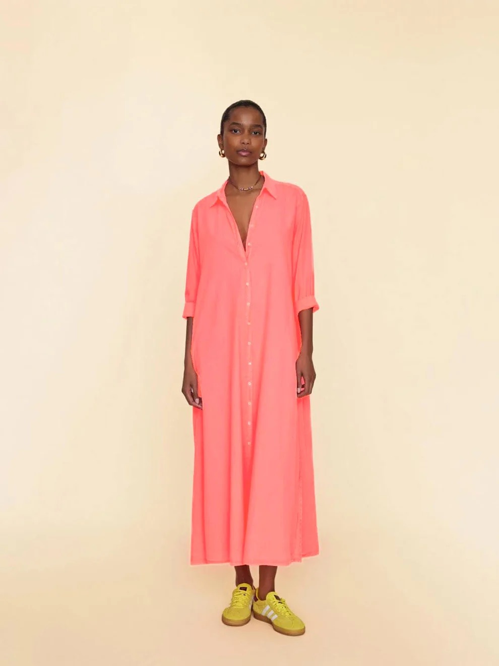 Woman standing in a coral dress paired with yellow sneakers against a neutral background.