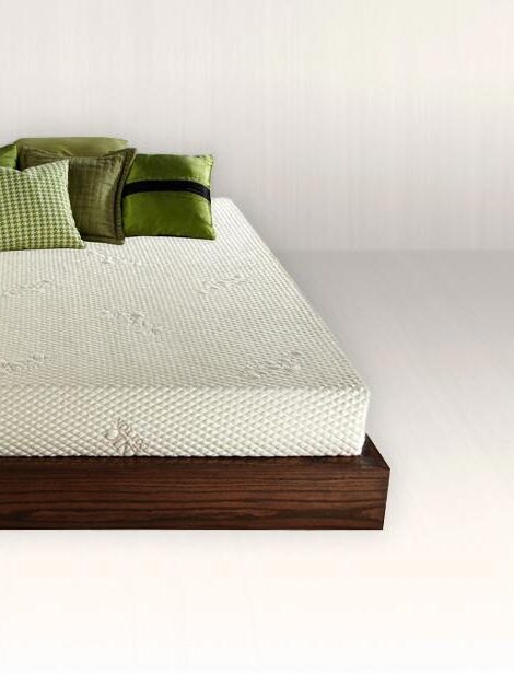 A modern bed with a dark wooden frame and white mattress, topped with green and white pillows, set in a white minimalist room.