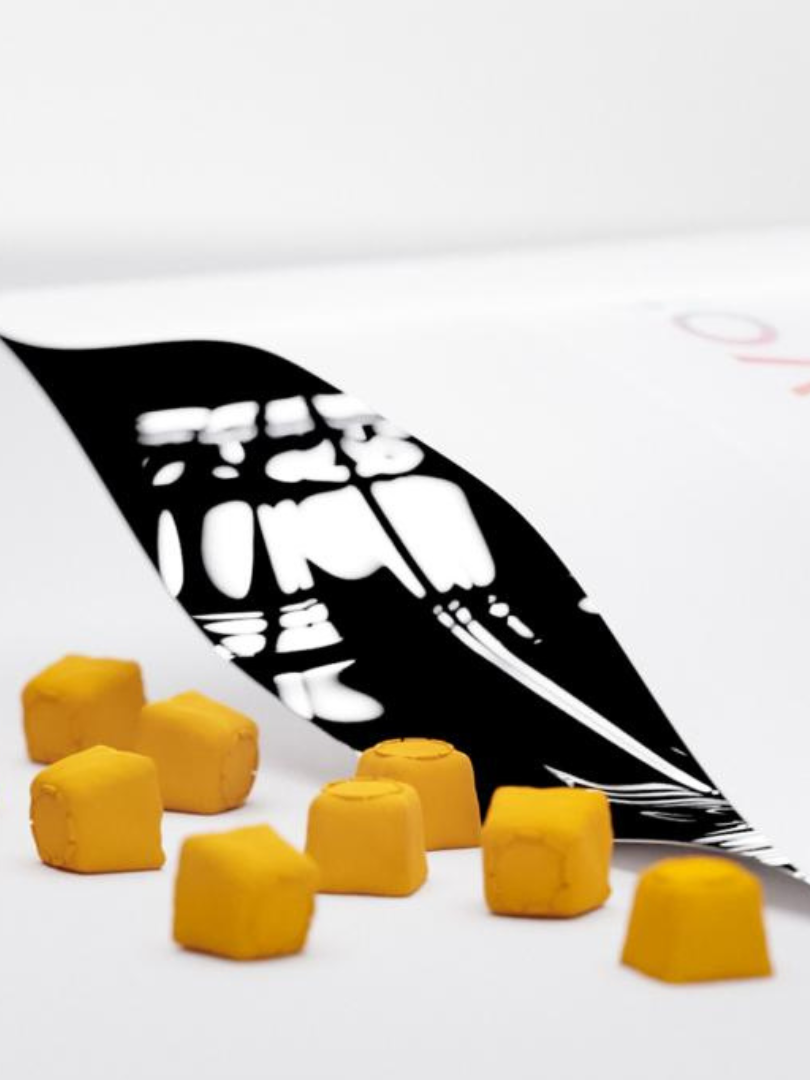 A white envelope partially reveals a black and white x-ray image, surrounded by scattered small yellow cubes on a white surface.