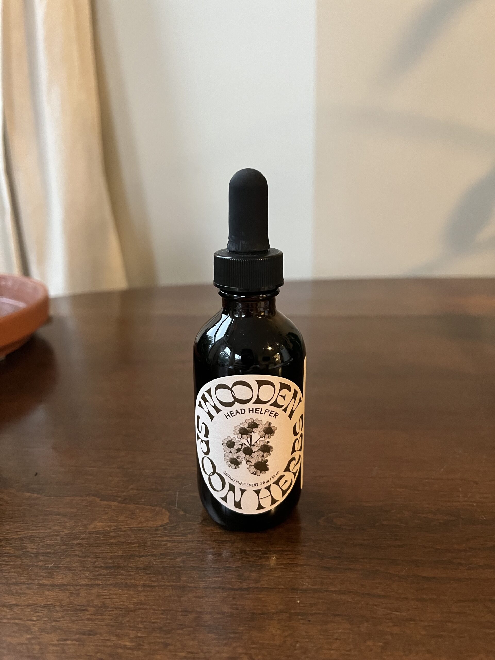 A glass dropper bottle labeled "Wooden Spoon Herbs" and "Head Helper" is placed on a wooden surface.