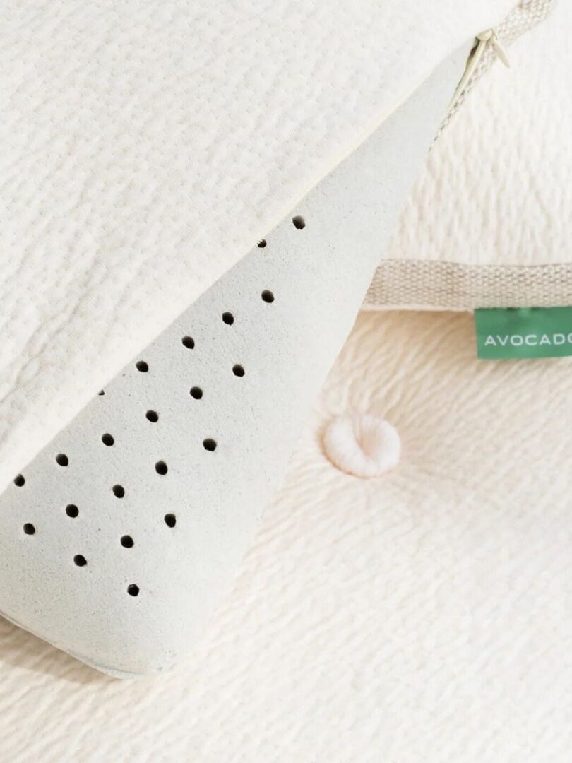 Close-up of a white pillow with a green tag labeled "Avocado." The pillow cover is partially open, revealing a perforated inner foam layer.