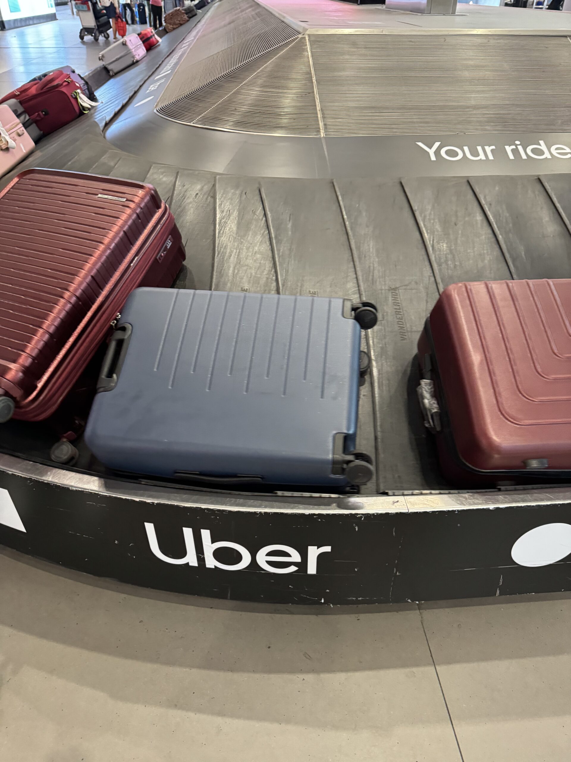 A blue suitcase and a red suitcase on an airport baggage claim belt. An Uber advertisement is visible on the belt.