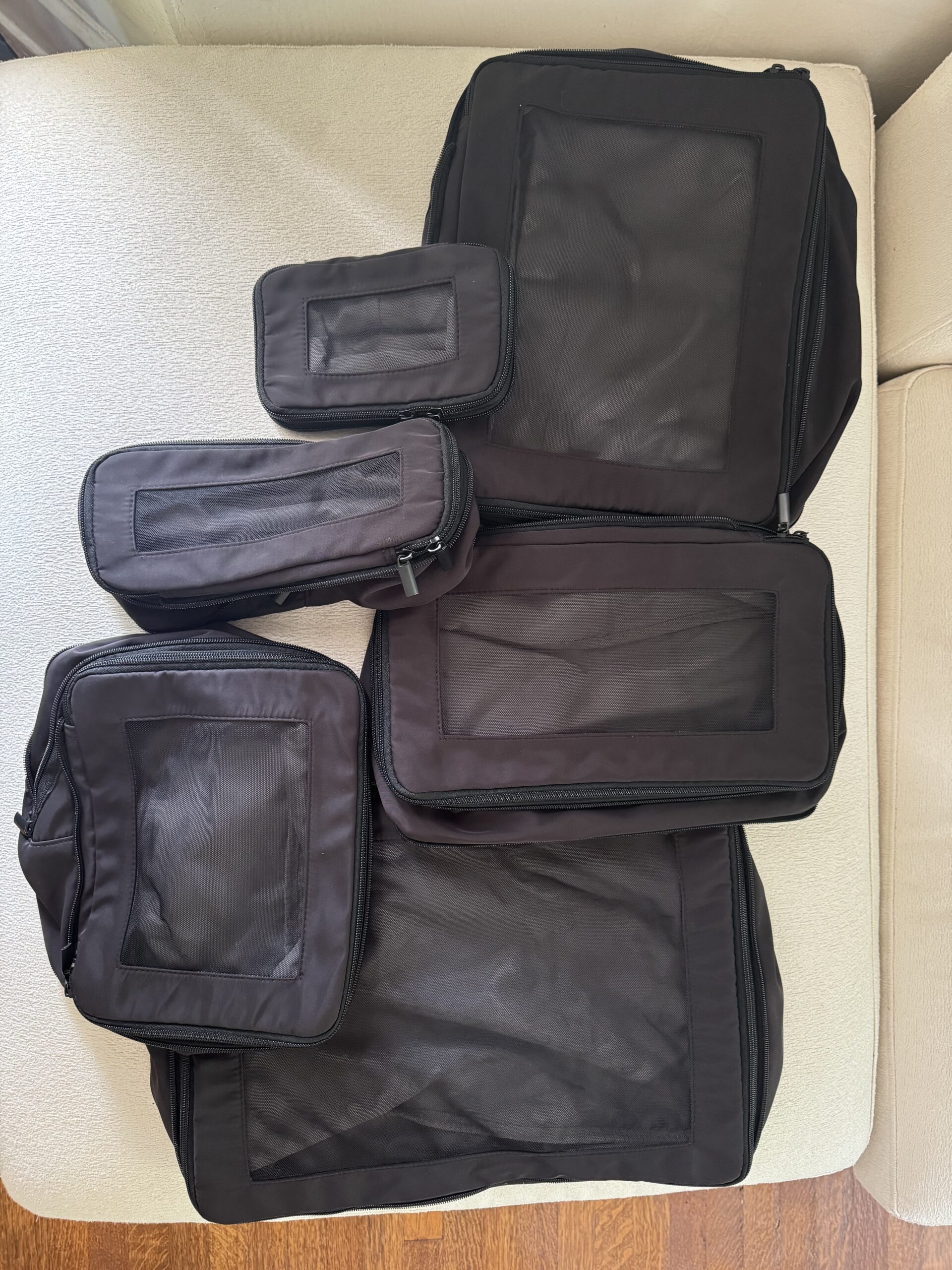 A set of five black packing cubes of various sizes, each with a mesh top panel, displayed on a light-colored surface.