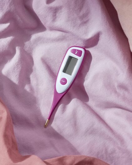Digital thermometer with a pink and white design resting on a pink fabric surface.