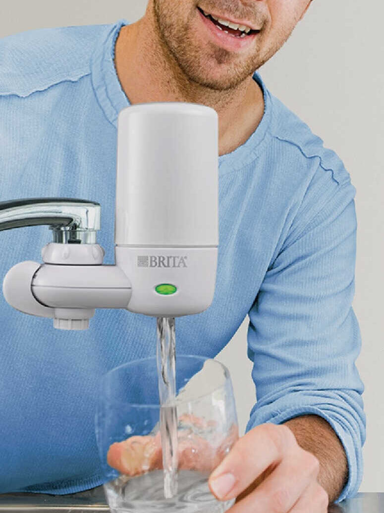 A man is filling a glass with water from a Brita faucet filter attached to a kitchen tap. The image includes text reading, "Great-tasting filtered water, right from your tap.