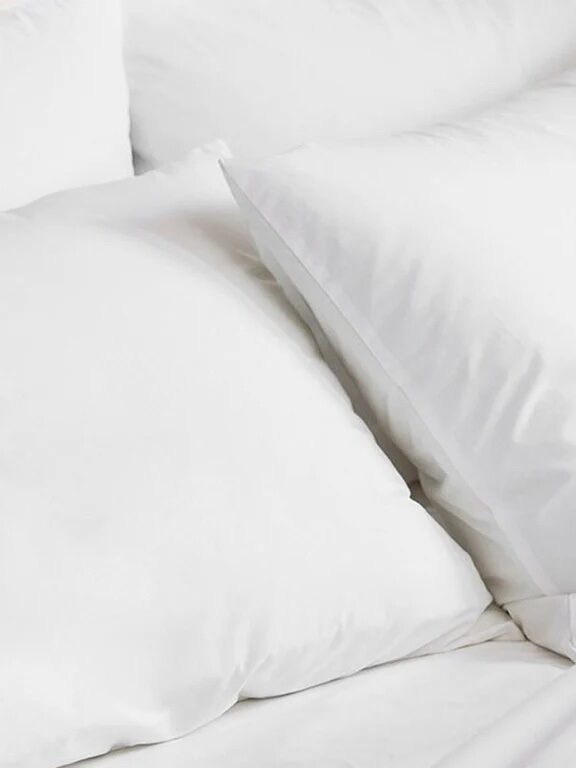 A close-up image of four fluffy white pillows and part of a white bedspread, arranged on a bed.