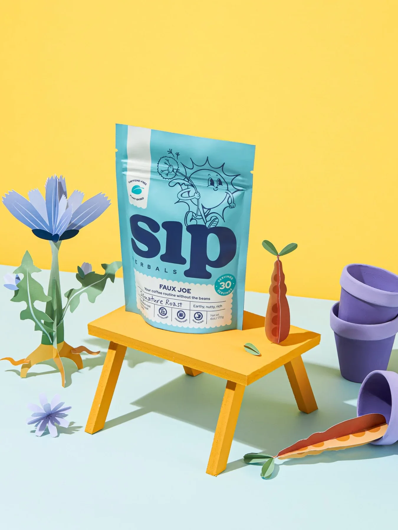 A blue package labeled "sip Herbals" sits atop a small yellow table. Surrounding it are decorative flowers, mini purple pots, and carrots. The background is a combination of yellow and light blue.
