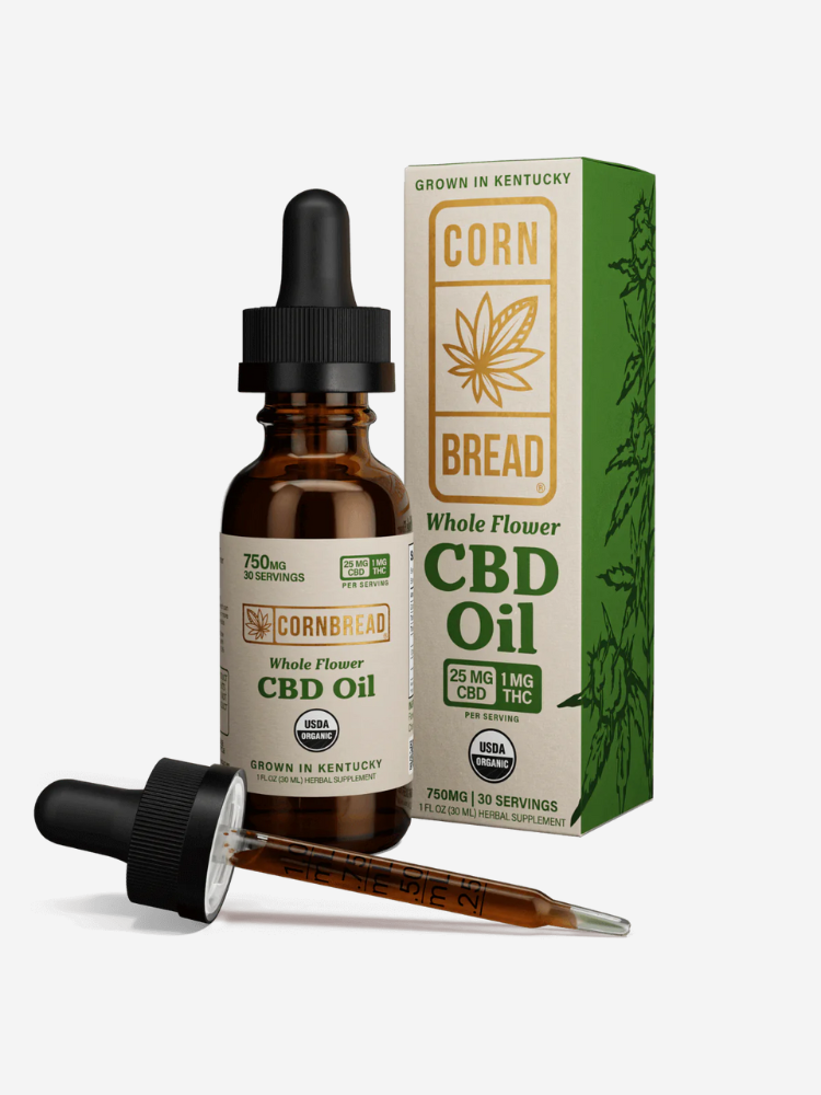 A bottle and box of Cornbread Whole Flower CBD Oil, labeled as containing 750mg, 30 servings, with a dropper lying beside it. The packaging indicates it is grown in Kentucky and USDA certified organic.