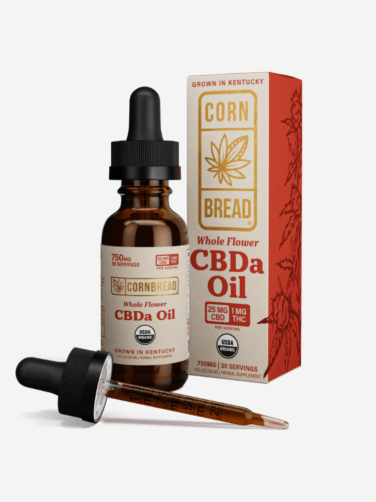 A bottle of Cornbread Whole Flower CBDa Oil with a dropper beside it and its packaging box in the background, showing product details such as 25 mg CBD and 1 mg THC per serving.
