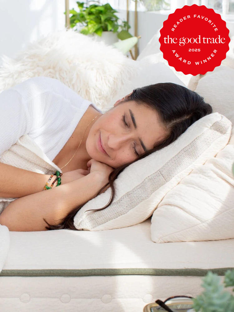 Person sleeping on a bed with white sheets and a fluffy pillow, sunlight streaming in. A "The Good Trade 2025 Reader Favorite Award Winner" badge is displayed in the top right corner.