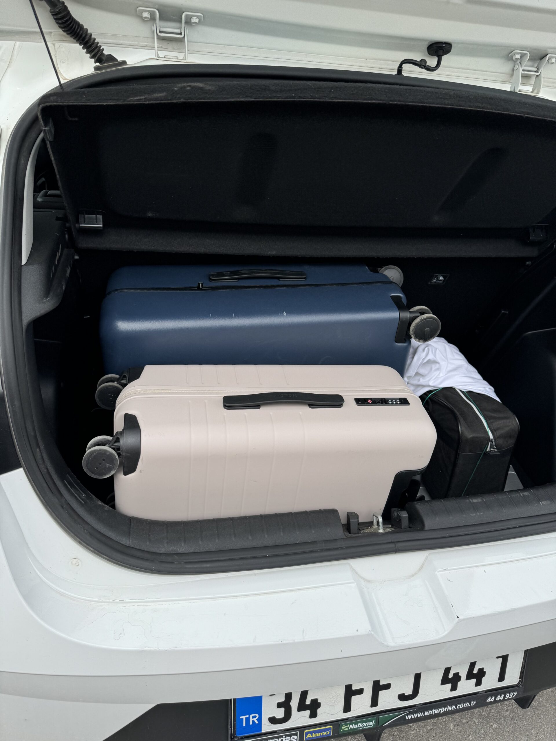 An open car trunk containing blue and white suitcases along with a small rectangular black bag and a white cloth.
