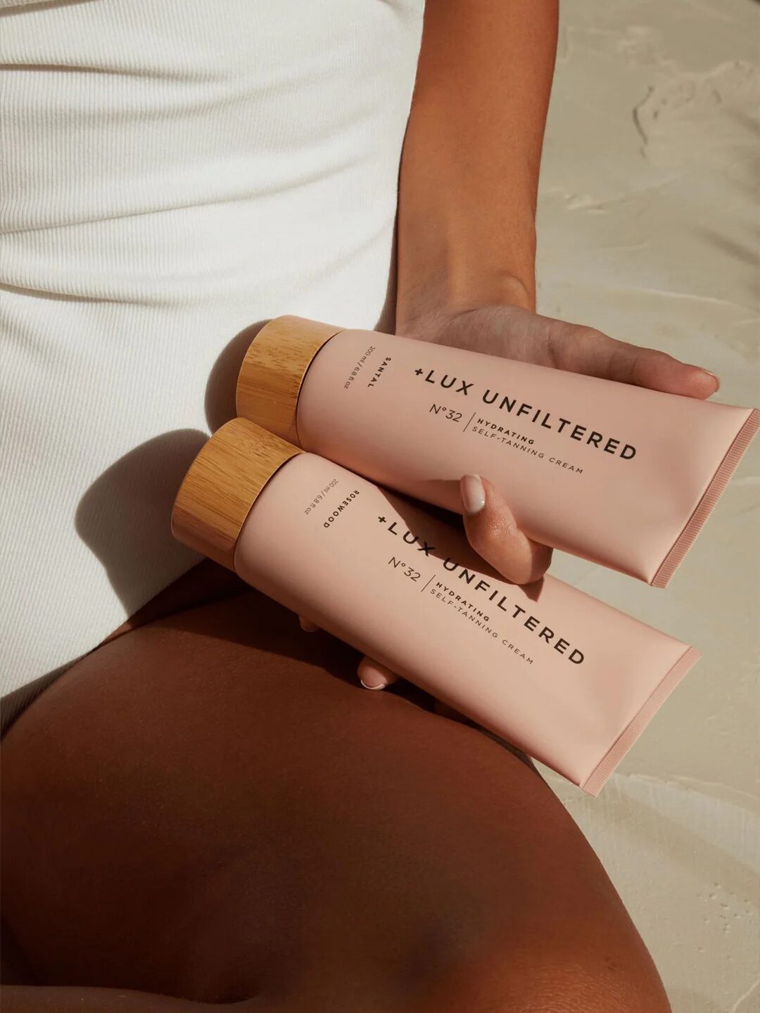 Person in a white outfit holding two pink bottles labeled "+LUX UNFILTERED.