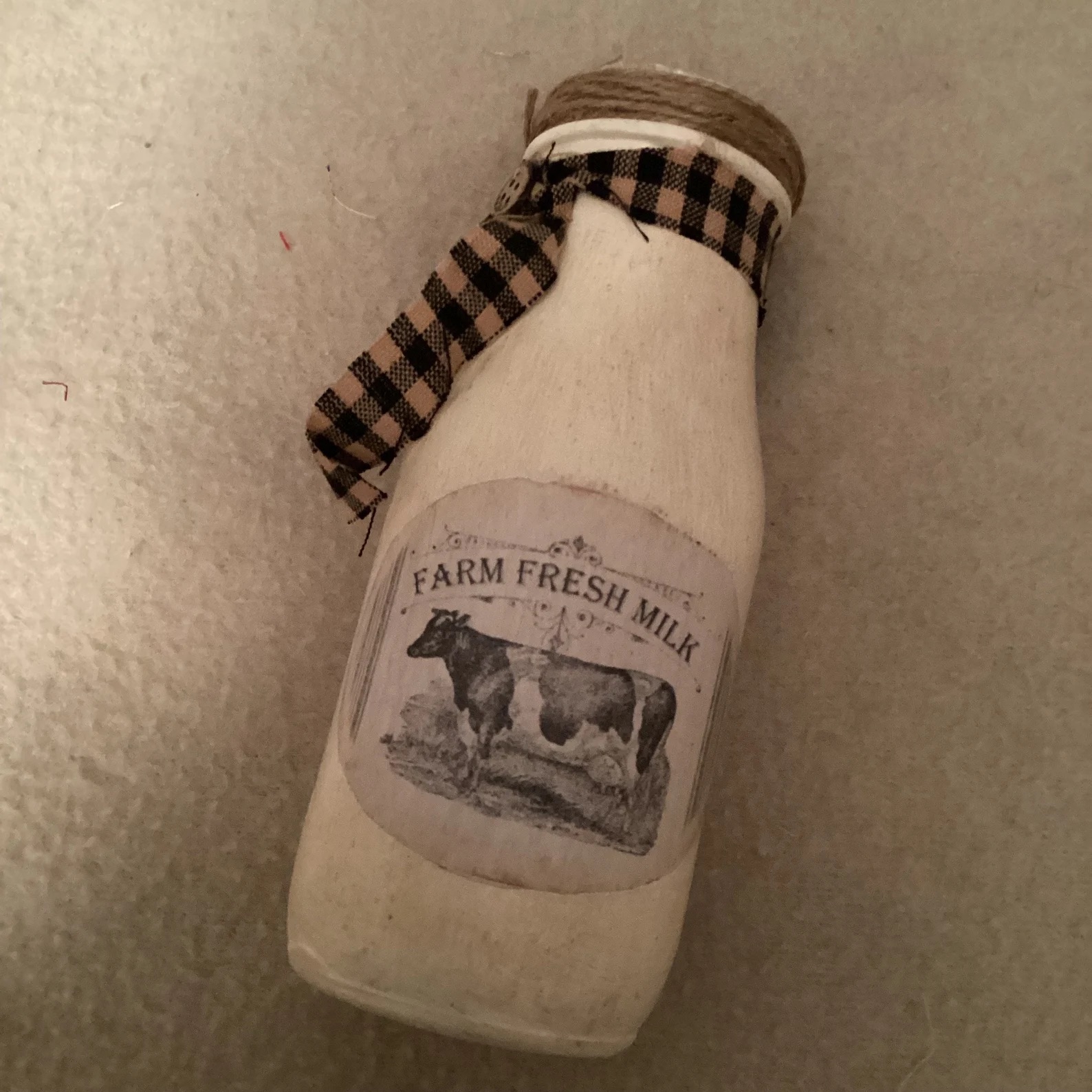 A small vintage-style bottle with a label featuring a cow and text "Farm Fresh Milk." The bottle is tied with a black and white checkered ribbon at the neck.