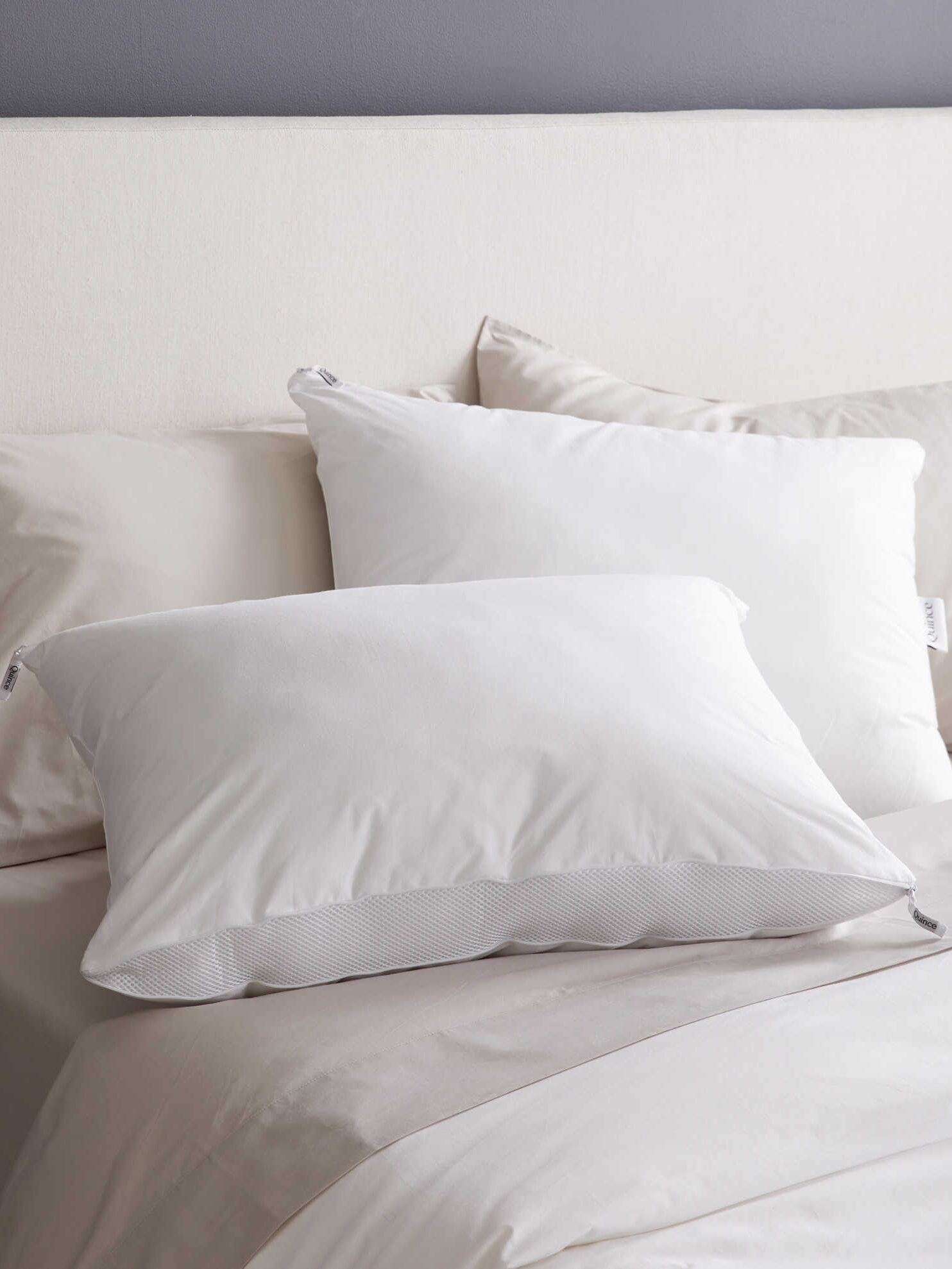 Two white pillows on a neatly made bed with beige sheets and a light-colored headboard in the background.