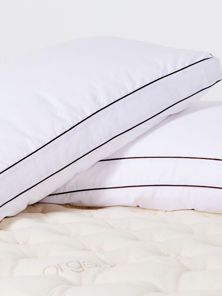 Two white pillows with dark trim lie on a quilted mattress. One pillow is stacked on top of the other at an angle.